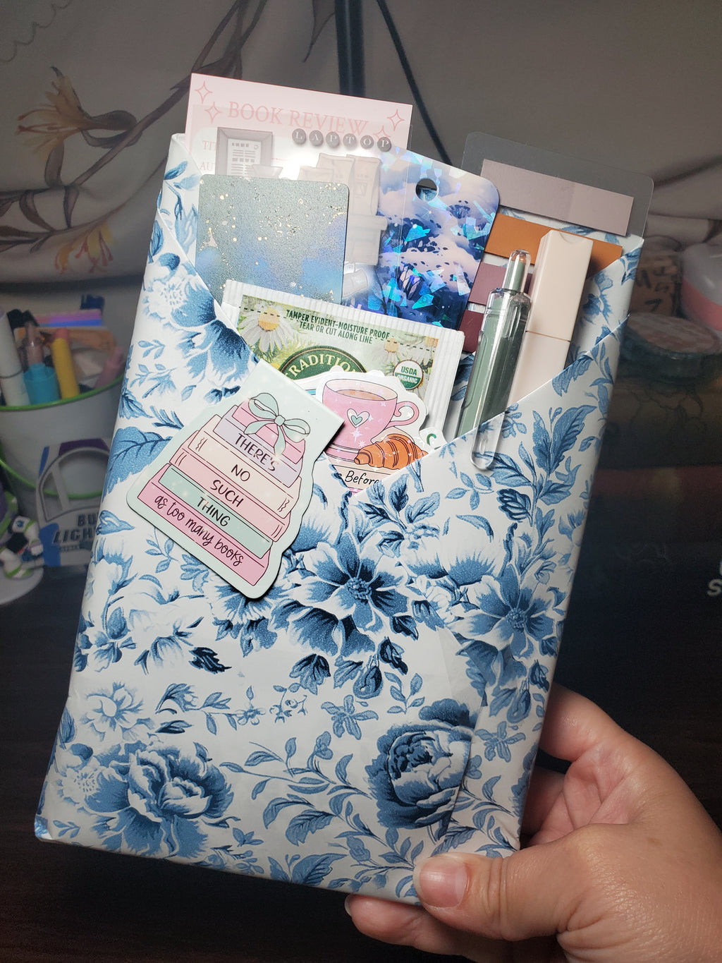 Blind Date With a Book wrapped in blue and white floral paper, with a chamomile tea bag, bookmarks, pen, marker, annotation tabs, and book-themed stickers tucked inside