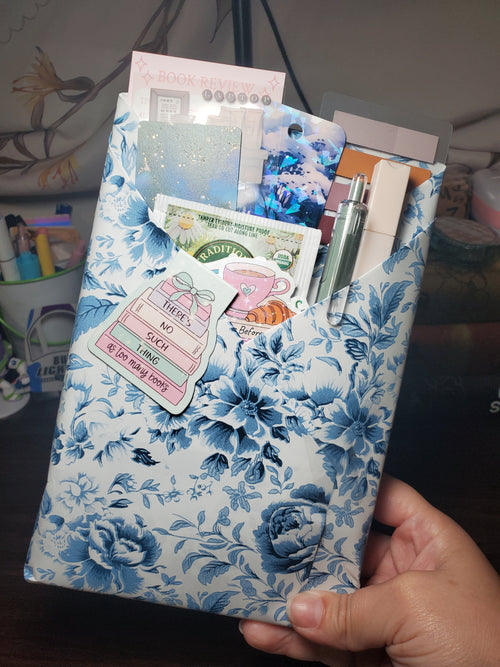Blind Date With a Book wrapped in blue and white floral paper, with a chamomile tea bag, bookmarks, pen, marker, annotation tabs, and book-themed stickers tucked inside