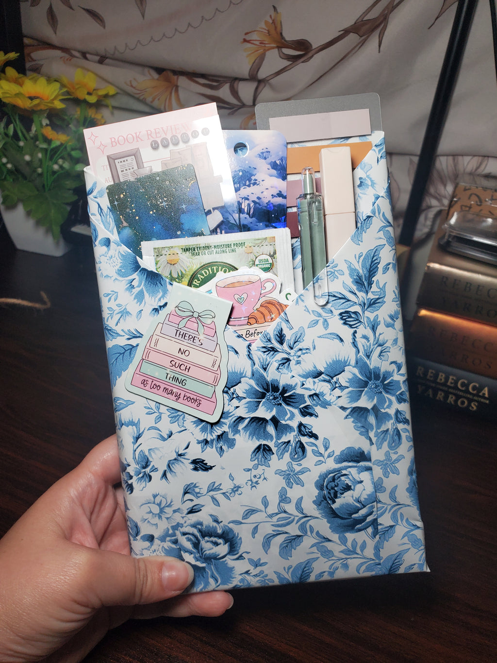 Overhead view of a blue and white floral wrapped Blind Date With a Book bundle with bookmarks, chamomile tea, pen, and stickers peeking out of the top